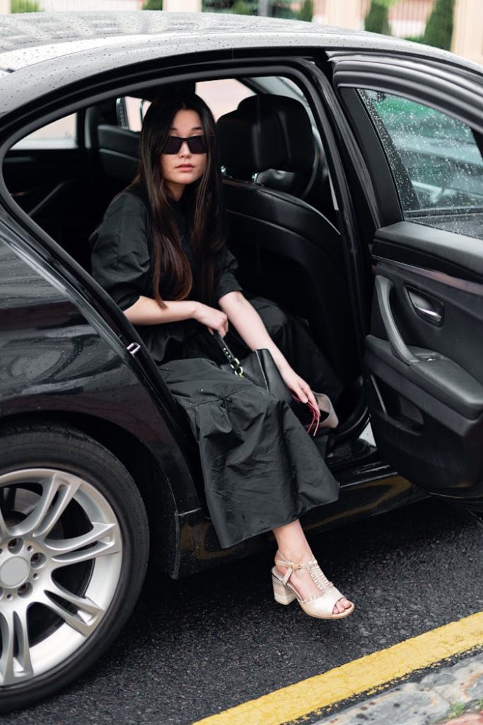 Chic woman in sunglasses and black dress gracefully stepping out of a luxury car.