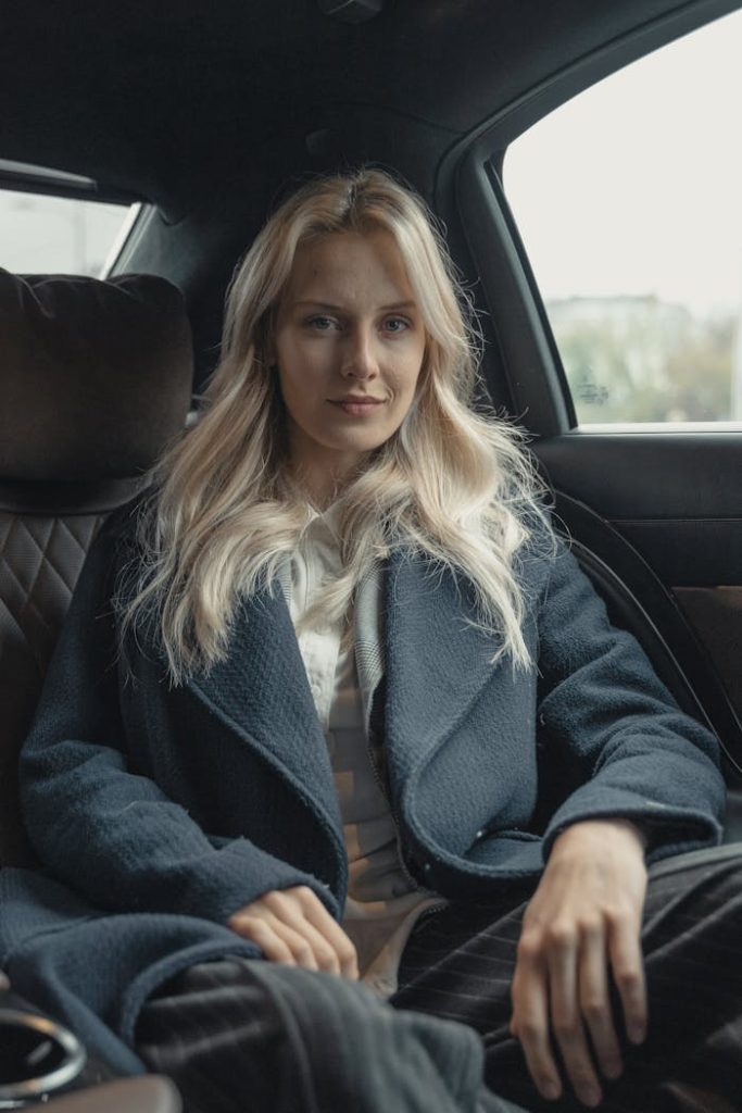 Blonde woman sitting confidently in car, exuding professionalism and poise.